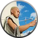 Man in beige shirt checking his phone outdoors with blue sky and construction crane behind him.